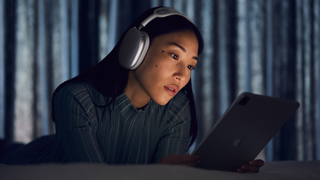 AirPods Max worn by a woman, in a darkened room, who is watching content on a tablet