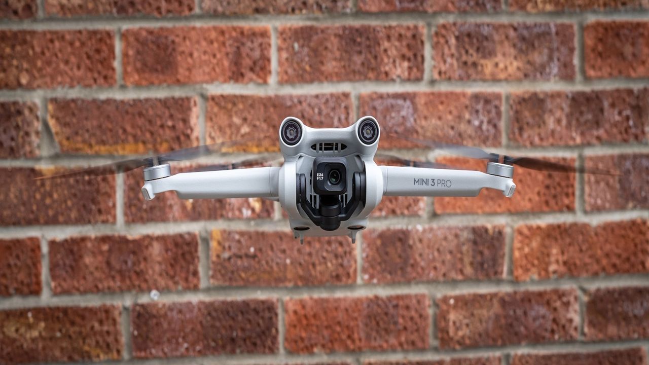 DJI Mini 3 Pro Drone hovering in front of a red brick wall.