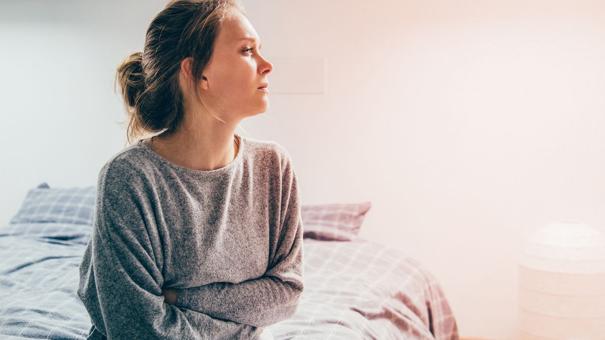 woman sat on her bed holding her stomach