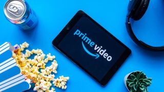 Prime Video logo appears on a tablet surrounded by a can of soda, spilled popcorn, headphones and a cactus