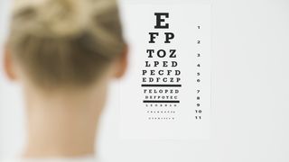 A woman with blonde hair looks at an eye test chart on a white wall