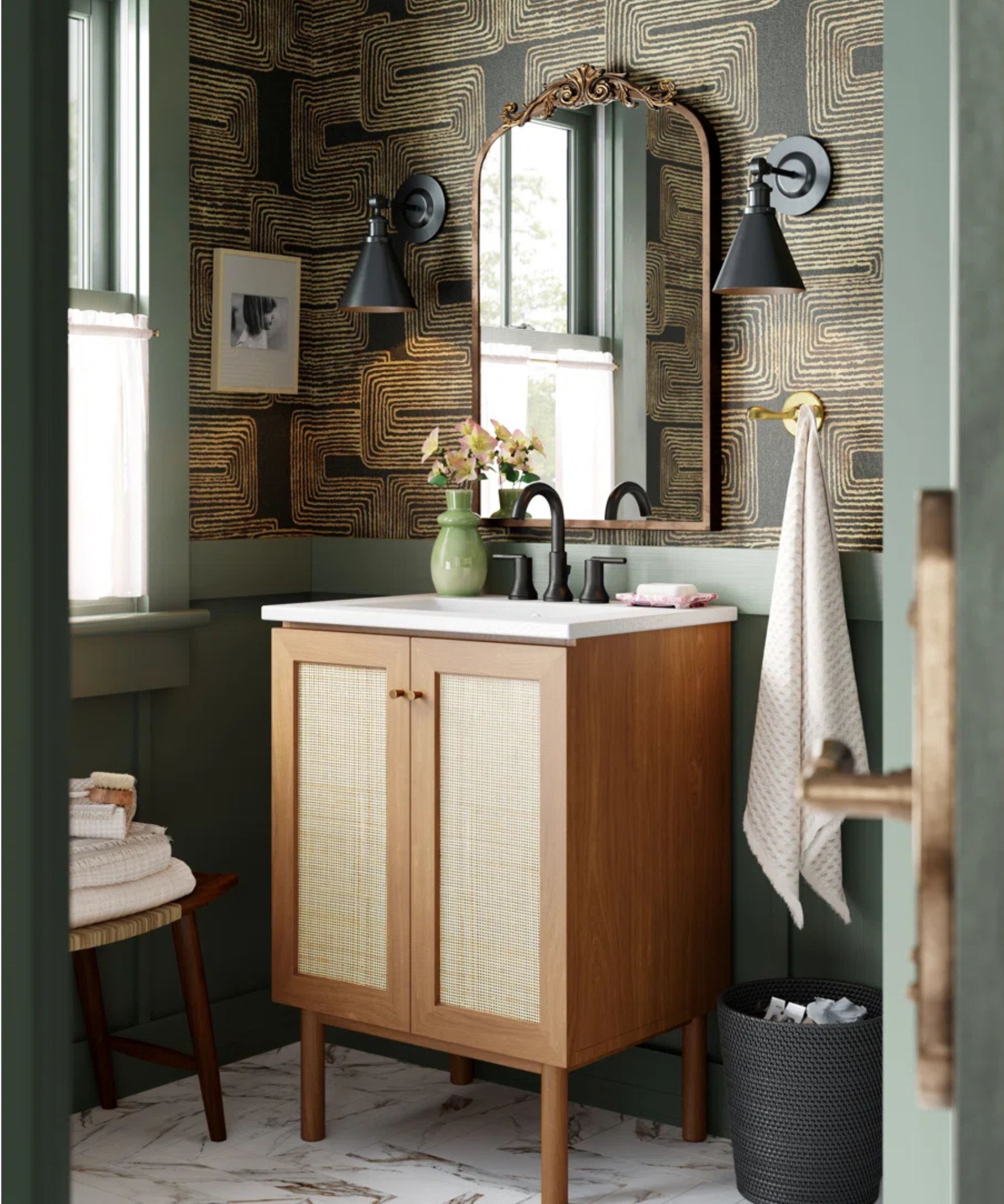A Mid-century style bathroom vanity in a small bathroom with green wallpapered walls and an ornate brass vanity mirror
