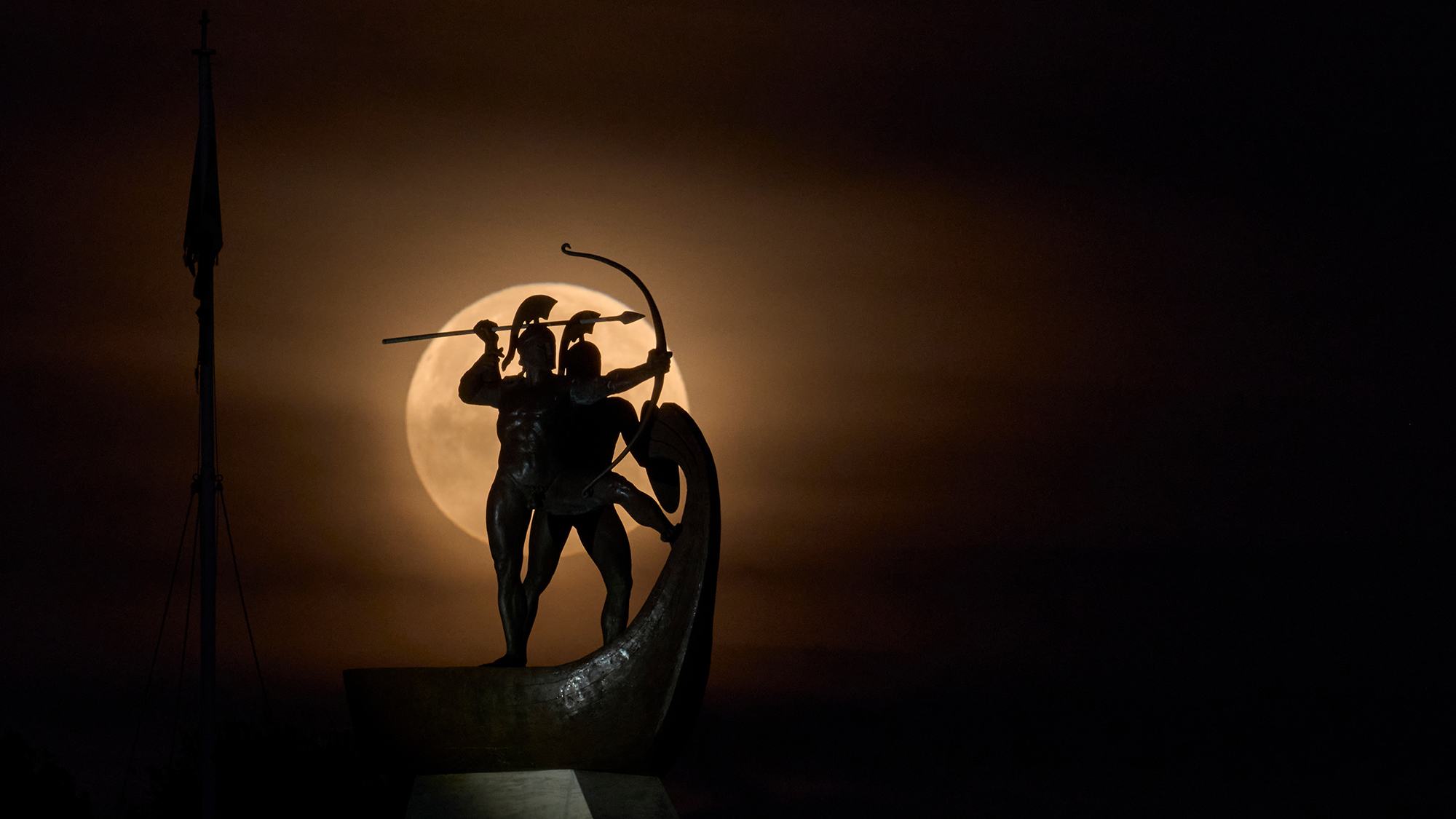 A full Worm Moon sets behind a monument at the Tomb of the Salamina Fighters on Salamis, Greece