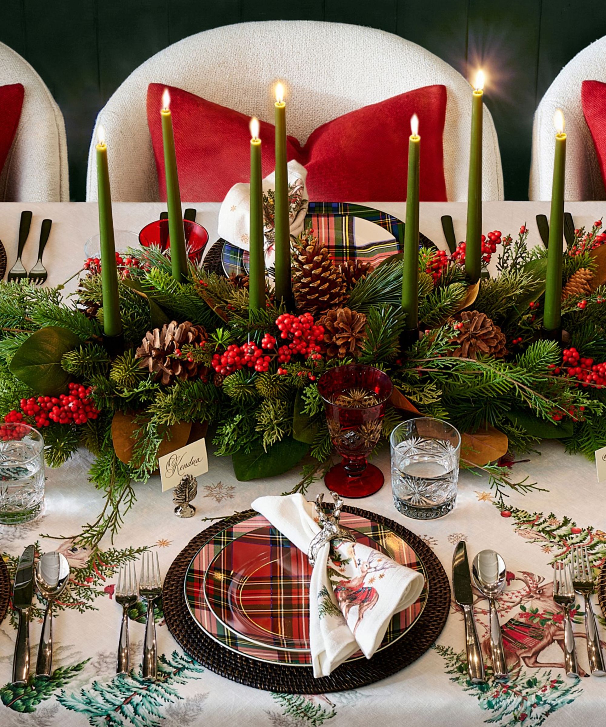 Christmas table with red plaid plates, green taper candles and a pine and berry centerpiece