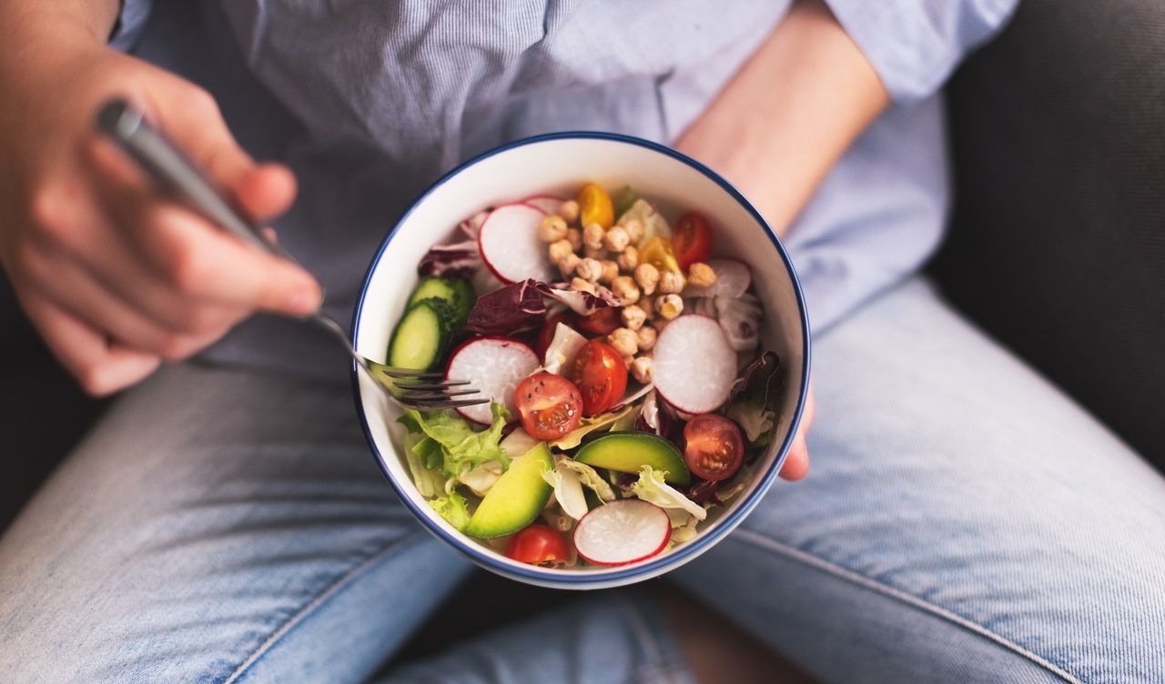 Green vegan breakfast meal in bowl with spinach, arugula, avocado, seeds and sprouts. Girl in leggings holding plate with hands visible, vegan for beginners