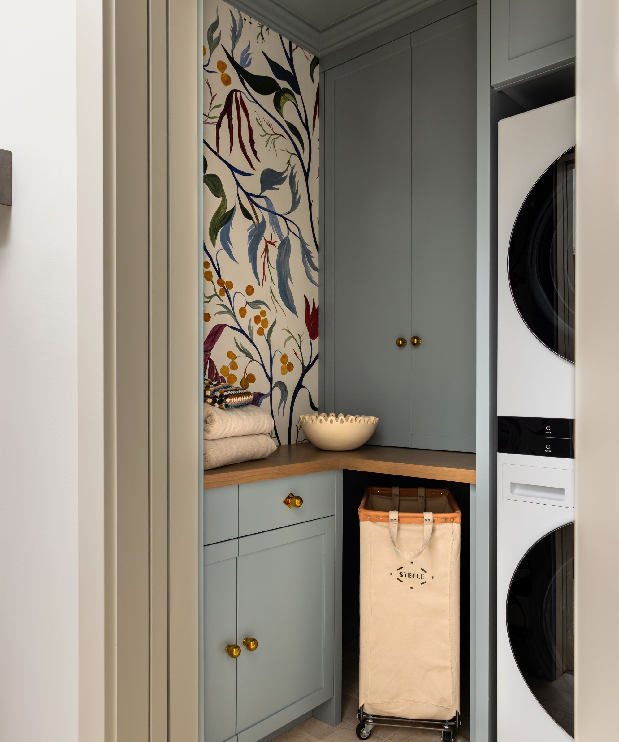 Small laundry room with blue cabinets, stacked washer dryer and a feature wallpaper