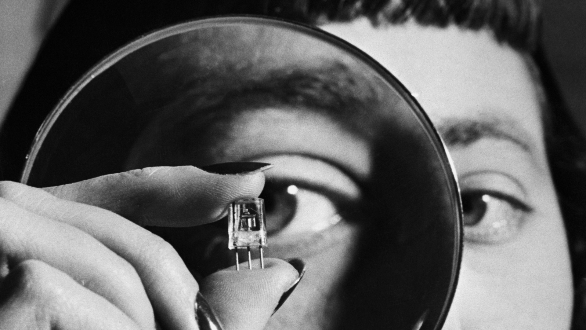 A 1952 close-up photograph of an RCA lab technician using a magnifying glass to inspect a new transistor