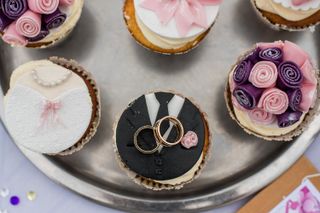 A selection of cupcakes artfully decorated and one with two wedding rings on top