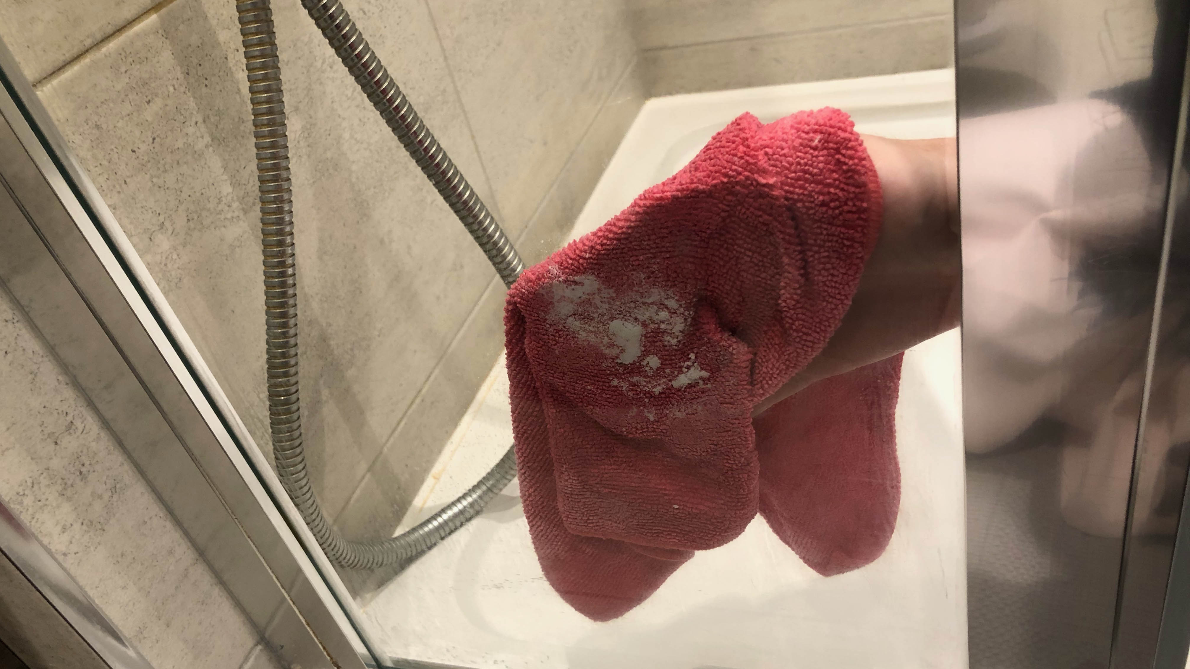 Someone is cleaning a glass shower panel with baking soda on a damp microfiber cloth.