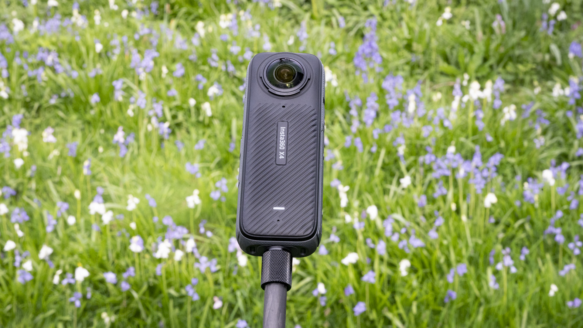 Insta360 X4 360 degree camera outdoors with vibrant grassy background on a selfie stick