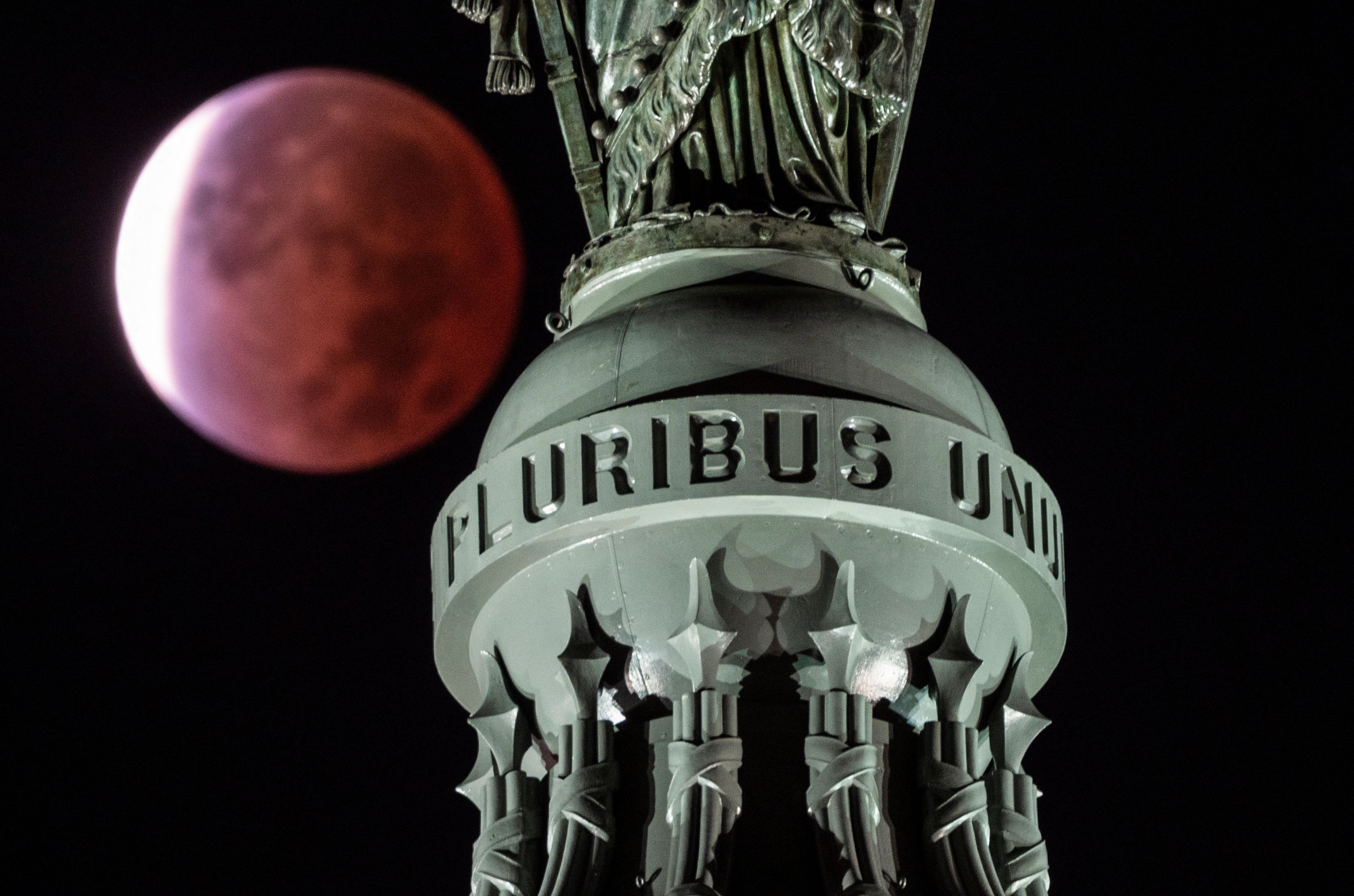 The moon, with a partial lunar eclipse, is seen behind the writing E Pluribus Unum, latin for "Out of many, one" on the Statue of Freedom at the top of the dome on Capitol Hill in Washington, DC early on November 19, 2021.