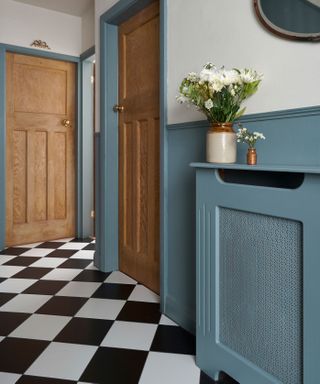 hallway with black and white floor tiles and powder blue walls with painted radiator cover