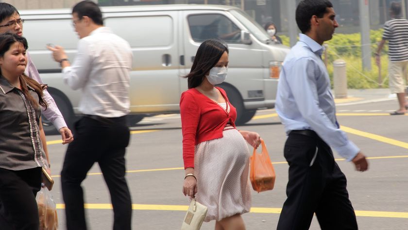 a pregnant woman walks across a busy street wearing a face mask