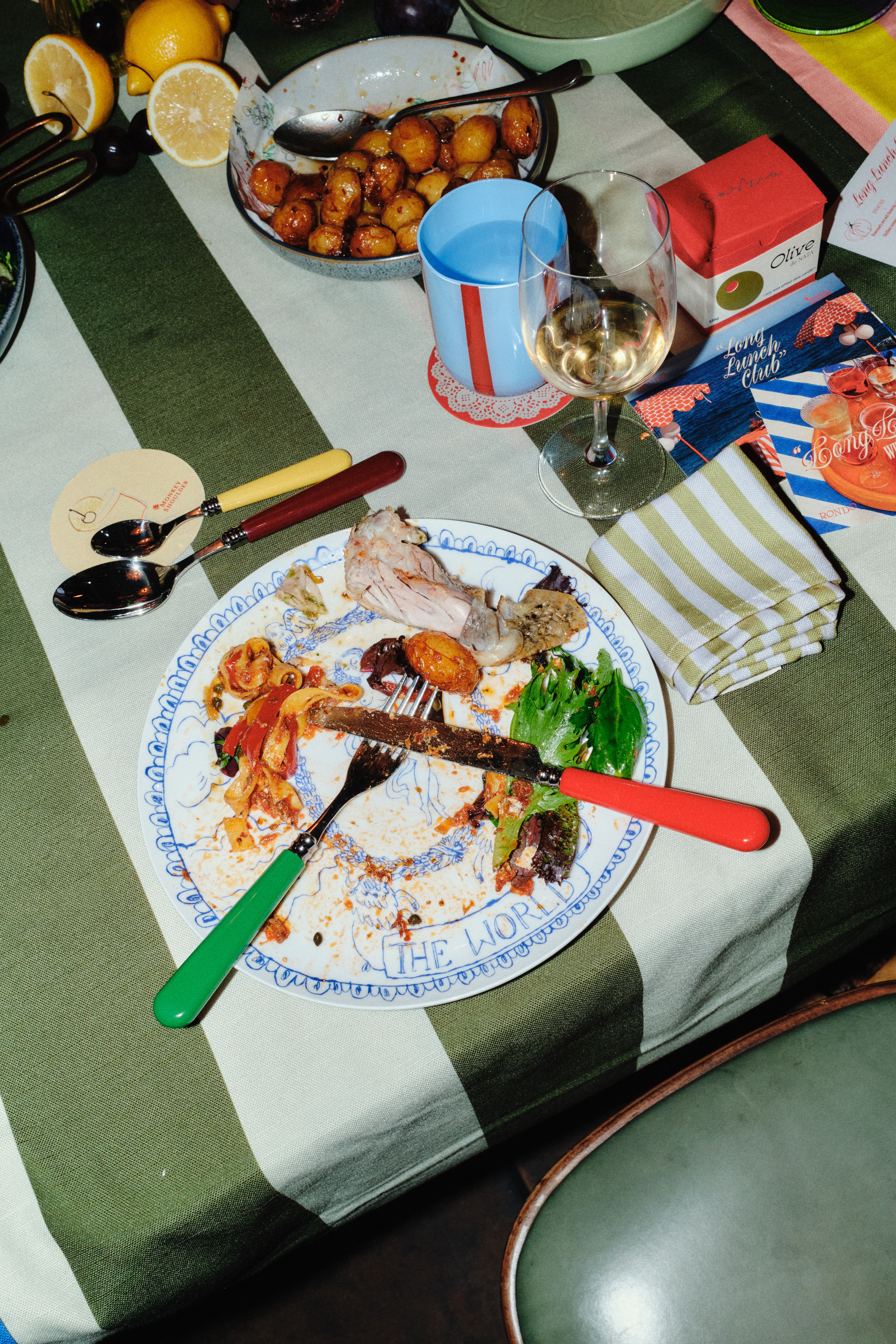 Flashed-out shot of a dinner party with silver and pastel-tinted serveware, beautifully presented dishes, striped, mismatched colorful table cloths, and branded merchandise.