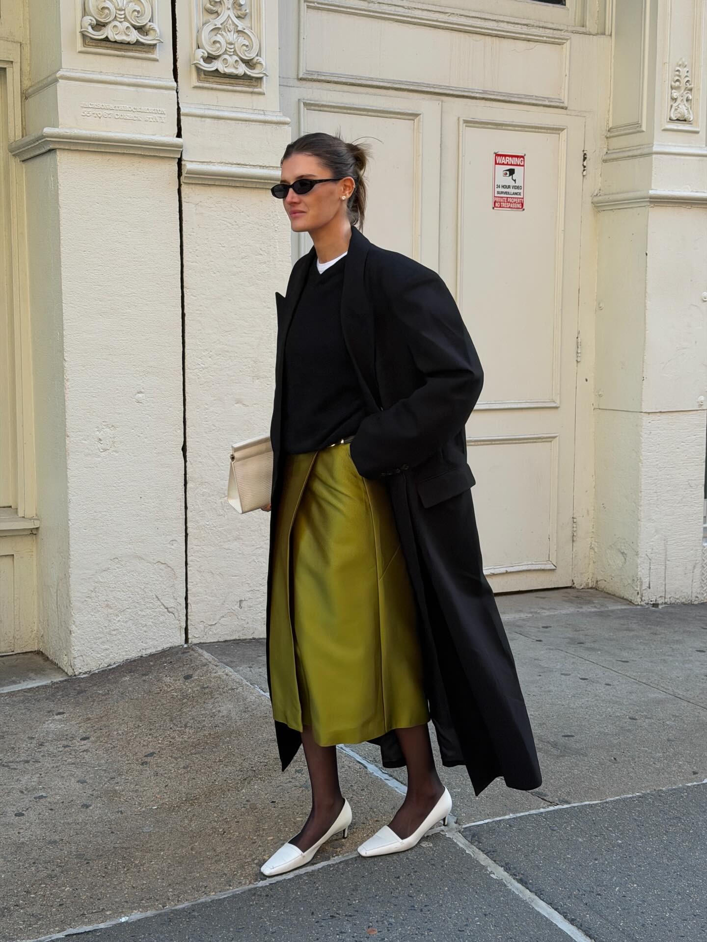 Influencer @cocoschiffer wears a chartreuse coloured skirt with white heels and a black wool coat.