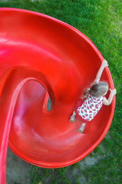 A girl climbs a bright red slide.