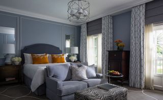Gray room with gray bed and white linen. A gray couch with a zebra ottoman. A modern light hanging from the ceiling.