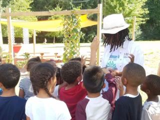 A person in a hat teaches children in a garden