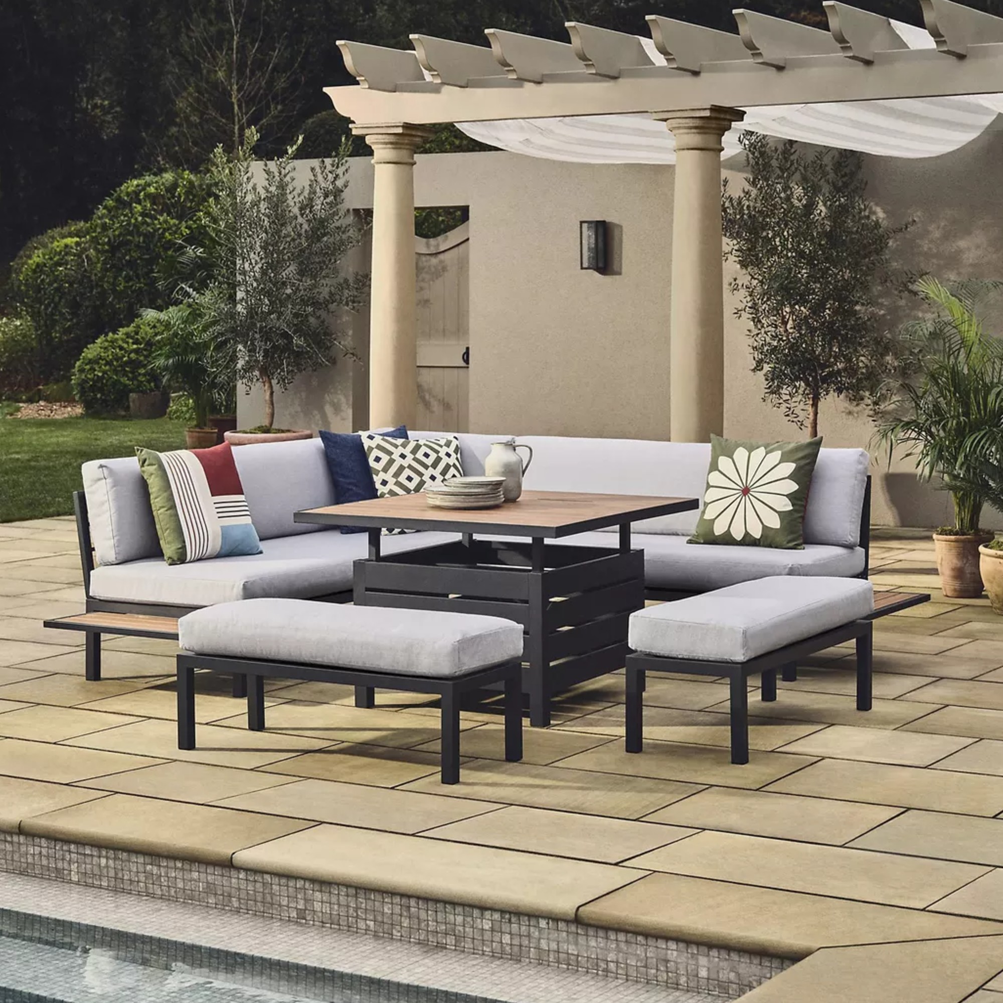 John Lewis Platform 8-Seater Corner Garden Dining Lounge Set with Height-Adjustable Table in grey next to an outdoor swimming pool
