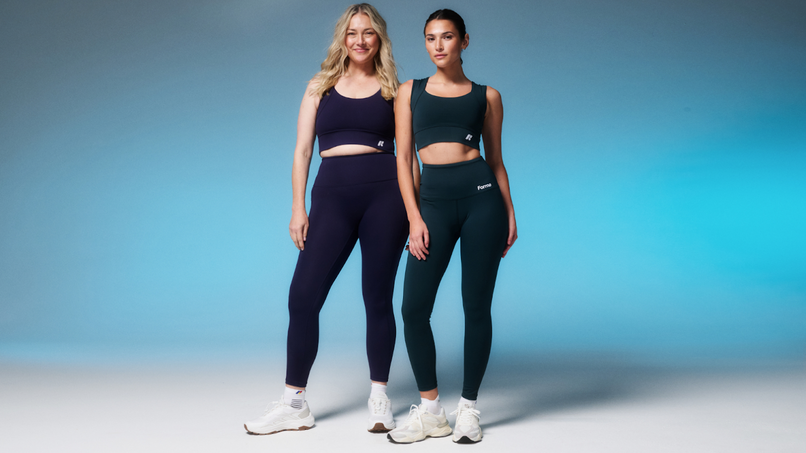 Two women wearing Forme activewear in dark blue and emerald green.