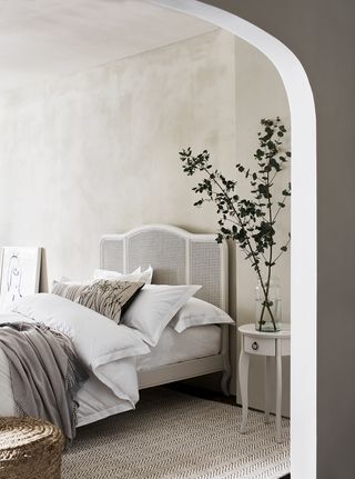 neutral bedroom with textured walls, herringbone rug, white side table, rattan bed, artwork