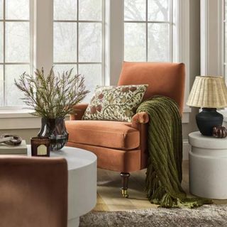 An orange armchair with a patterned pillow and green throw blanket