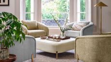 A seating nook in a white living room, with green and blue arm chairs situated around an upholstered cream ottoman.