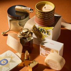 The best luxury beauty gifts for 2024 including Loewe Mimosa candle, Hermes Barenia soap, Tom Ford lip balm, Hourglass Ambient Lighting Edit, Jo Malone London Myrrh & Tonka, Sisley Gua Sha, Wildsmith Bath Salts and Dior Lipstick, intertwined with festive Christmas ribbon