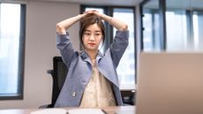 AI workslop concept image showing stressed female office worker with hands on head while working on laptop fixing low quality work. 