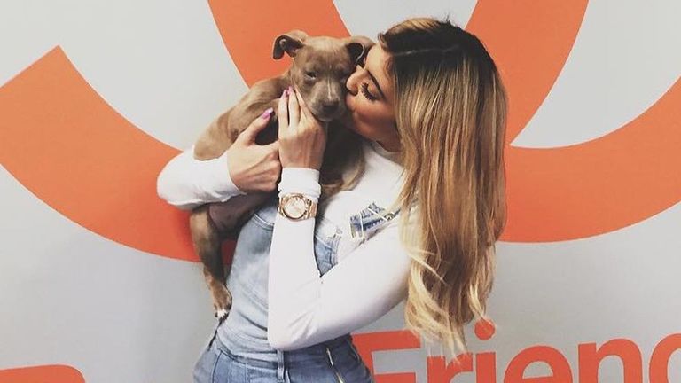 Kylie Jenner holds a puppy to her face and kisses its head.