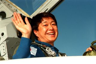 Chiaki Mukai smiles and waves from the cockpit of an airplane.