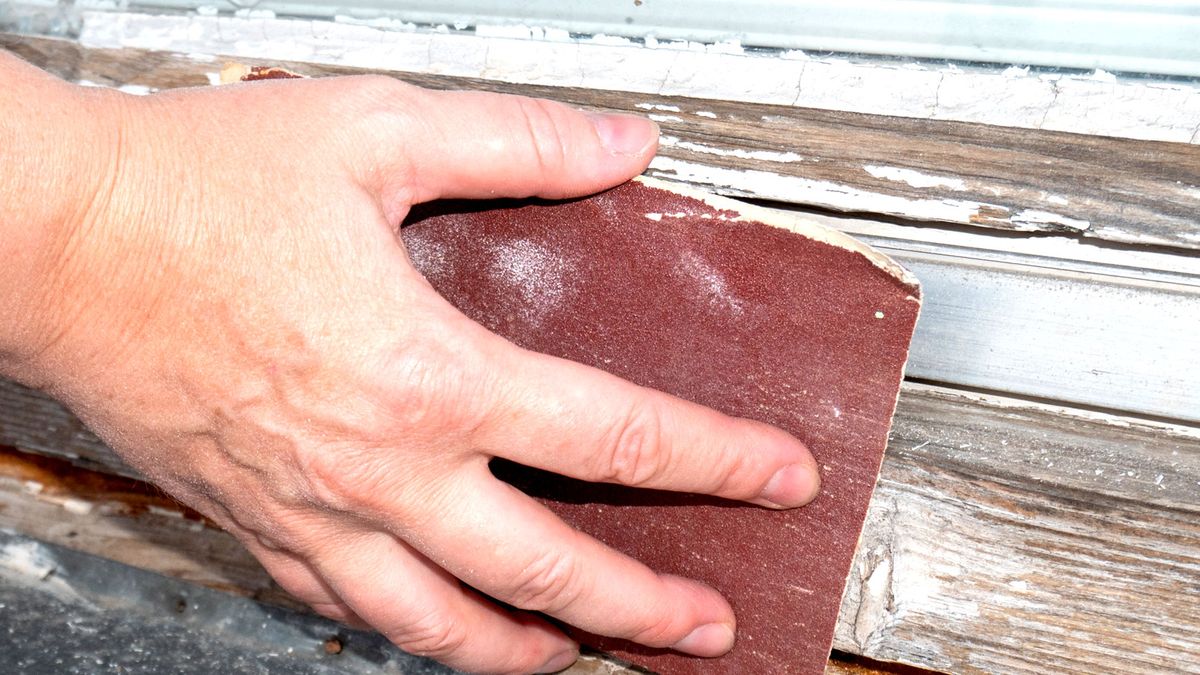 Close up of hand rubbing down old wooden window frame