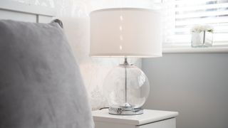 white lamp with glass base next to a gray bed in a light white bedroom