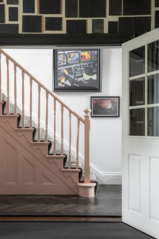 Hallway with dark parquet flooring, pink painted staircase railing and art on white walls