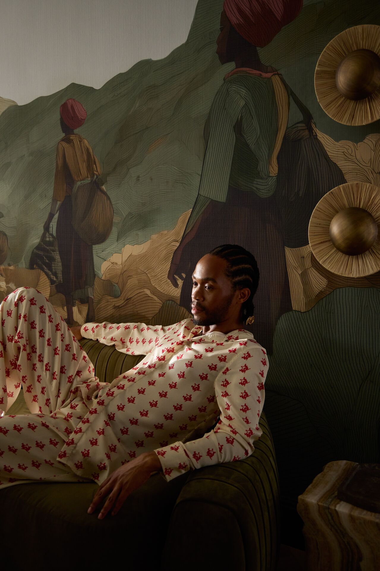 A series of shots capturing a young man dressed in patterned, or color-blocky, clothing, either standing in the sun-lit outdoor areas of a lush hotel, or inside a colorfully decorated suite filled with collectibles, artworks, and textural touches, or the interiors of that very space.