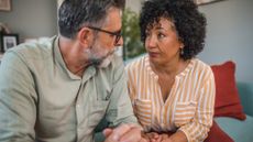 A middle aged couple have a serious talk on a sofa in the living room. 