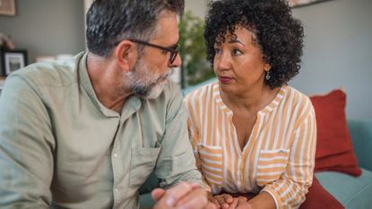 A middle aged couple have a serious talk on a sofa in the living room.