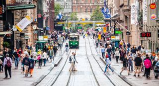 People cross a busy street during a sunny day in Helsinki, Finland