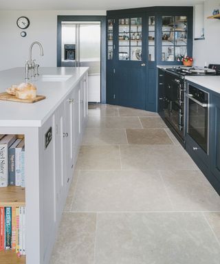 A dark blue pantry in the corner of a kitchen layout idea with travertine flooring.