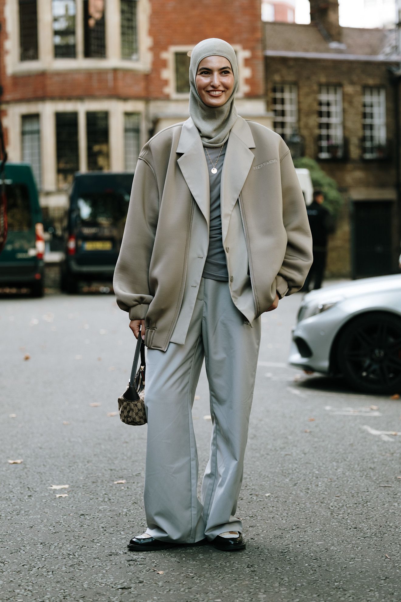 Person in a pair of grey trousers, a blazer, a coat, and a fitted blouse, wearing loafers.
