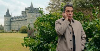 Rufus Sewell as Hal Wyler, talking on a phone while standing near a bush outside of a castle, in episode 204 of The Diplomat.