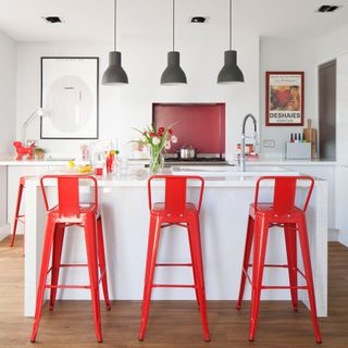 White kitchen with red bar stools and pendant lighting over island