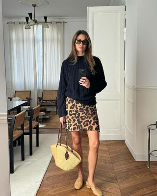 A influenciadora de moda francesa Anne Laure Mais em saia com estampa de leopardo, suéter azul marinho e bolsa cesta.