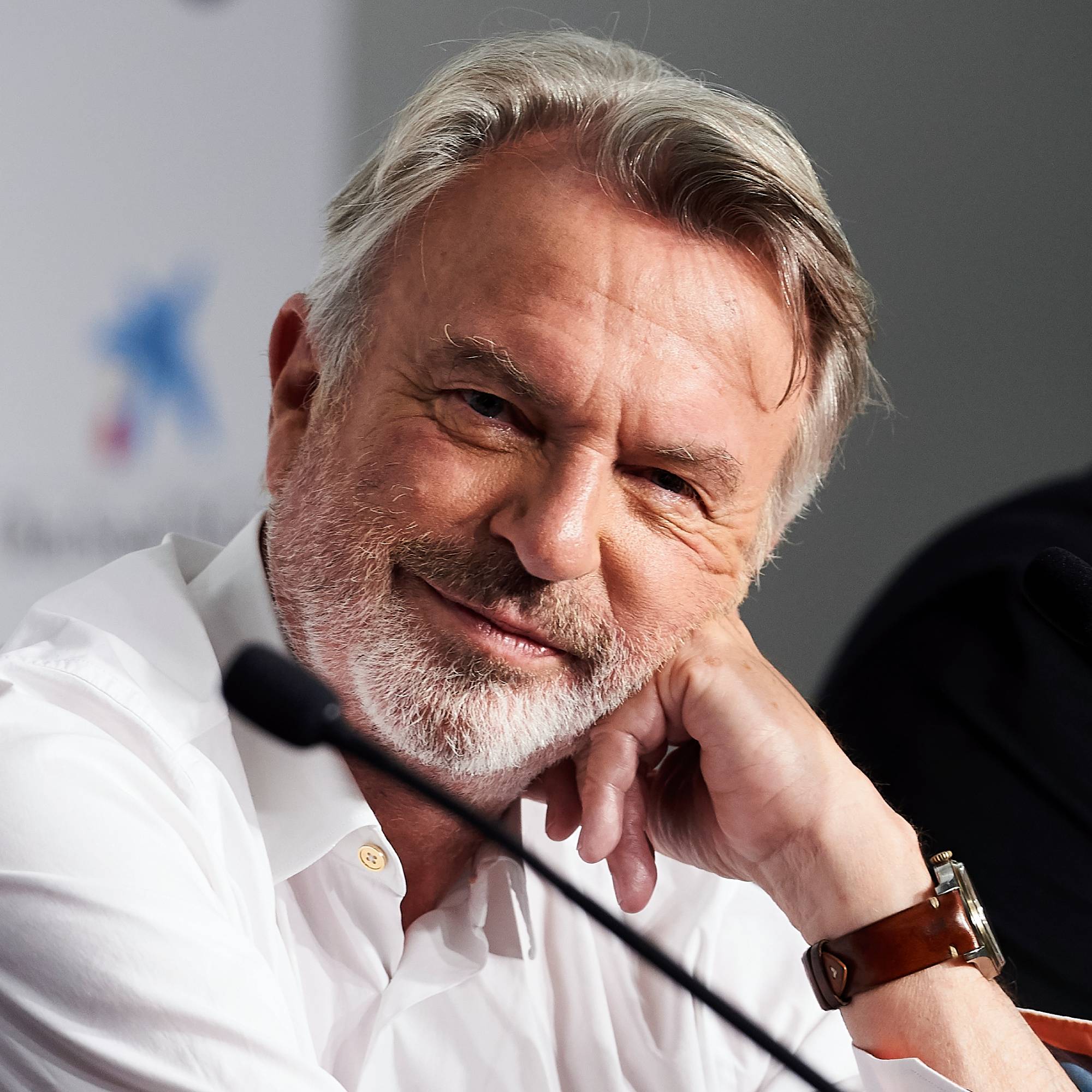 Sam Neill rests his head on his hand and looks toward the camera