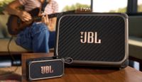 JBL's new BandBox amp and speaker sit on a wood table, with a guitarist playing in the background