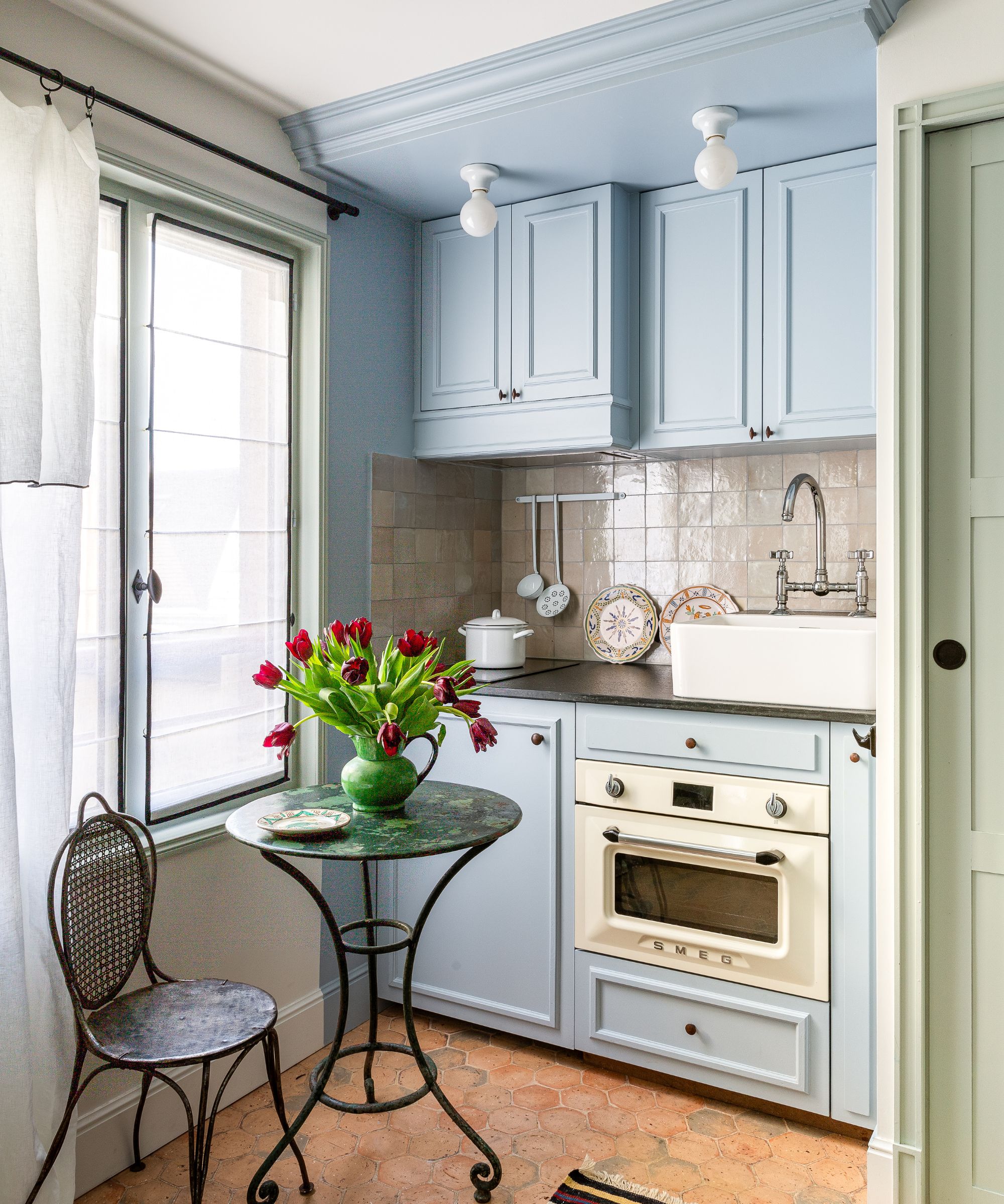 Small kitchen with pale blue cabinetry, terracotta tiled floor and wrought iron table and chairs