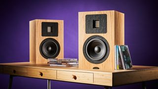 Neat Petite Classic standmount speakers on wooden desk in front of purple background