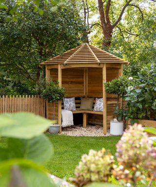 Elegant corner arbour with solid side panels and slatted roof design to allow light in and keep unexpected showers out