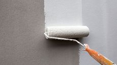 a person using one of the best paint rollers to paint white paint onto a gray wall