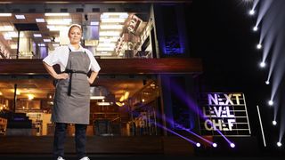 Contestant Jade in a white top and grey apron in front of the kitchen in Next Level Chef.